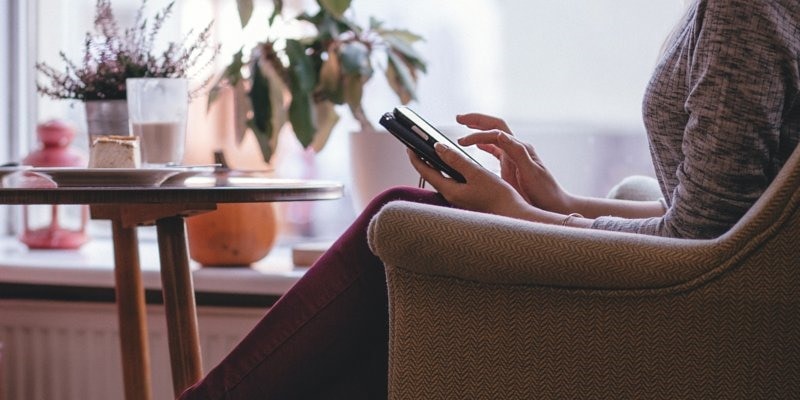 Woman browsing social media on her phone while sat in brown sofa chair