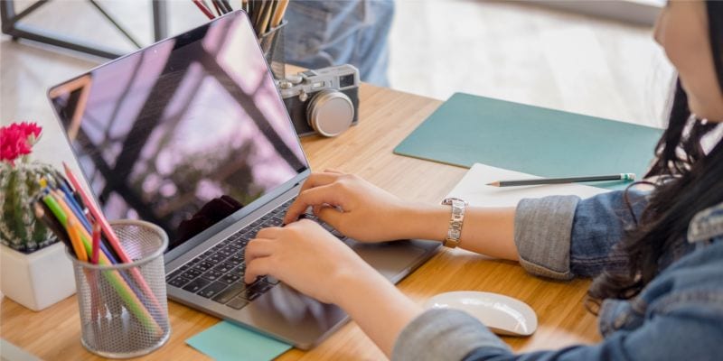 Girl using laptop at table Dark haired woman typing on laptop at desk