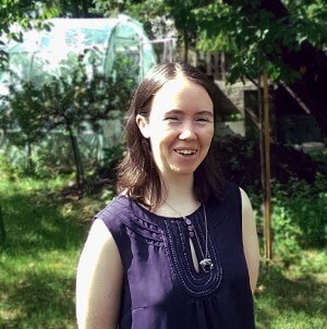 Photo of Lisa in a garden with lots of green trees and sunshine.