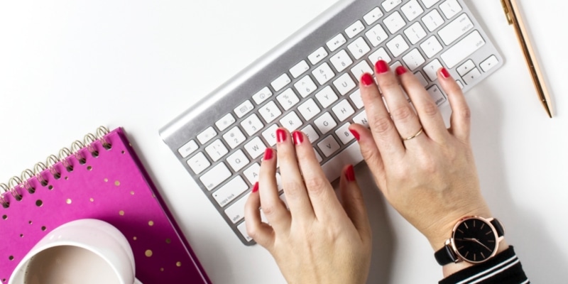 Blog Image Mistakes Of Woman Typing On Keyboard With Peach And Pink Flowers Mug And A Pink Notepad