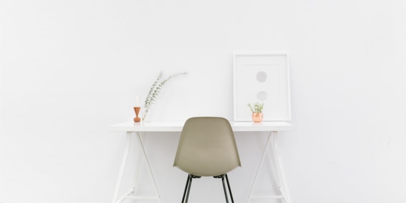 White Minimalist Desk With Coffee Colored Chair Against A White Wall