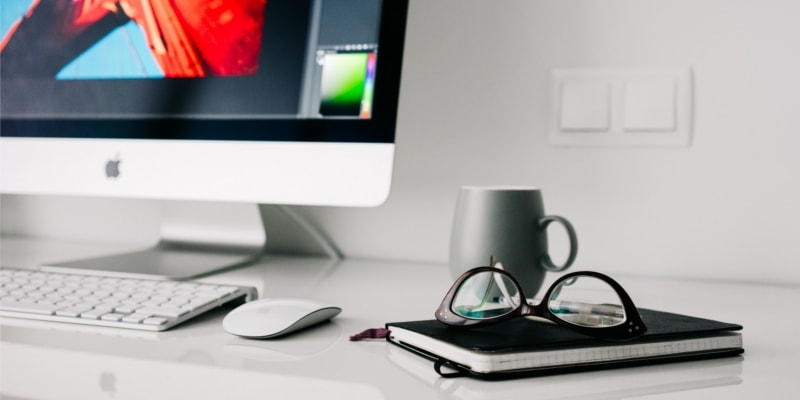 Mac And Computer Keyboard With Notebook Mug And Glasses On Top Of It