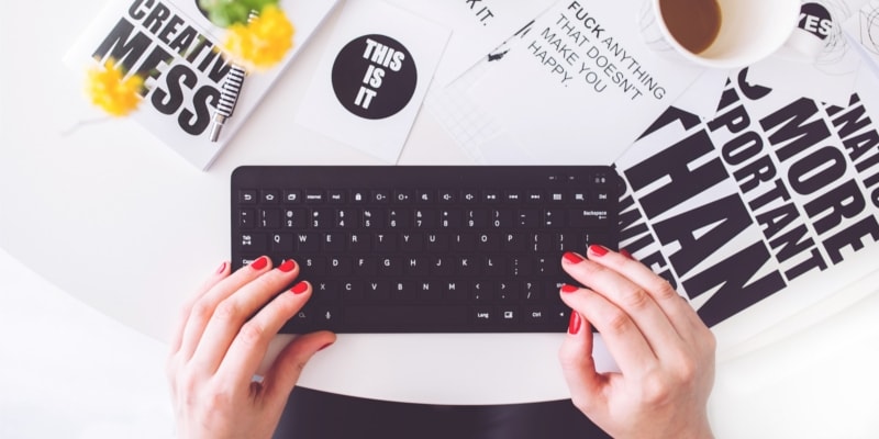 Female WordPress Blogger Using Mini Computer Keyboard With Lots Of Typography A White Mug Of Coffee And Some Yellow Flowers