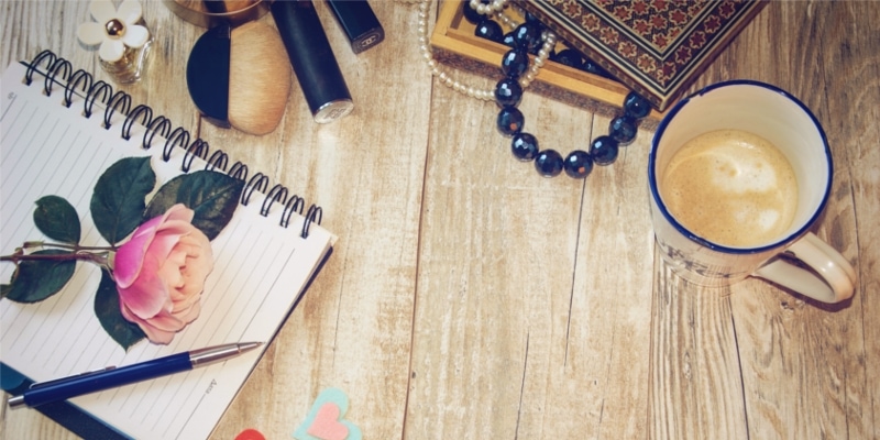 Blogging Notebook And Coffee Supply With Flowers Blue Beads And Other Items On A Wooden Table