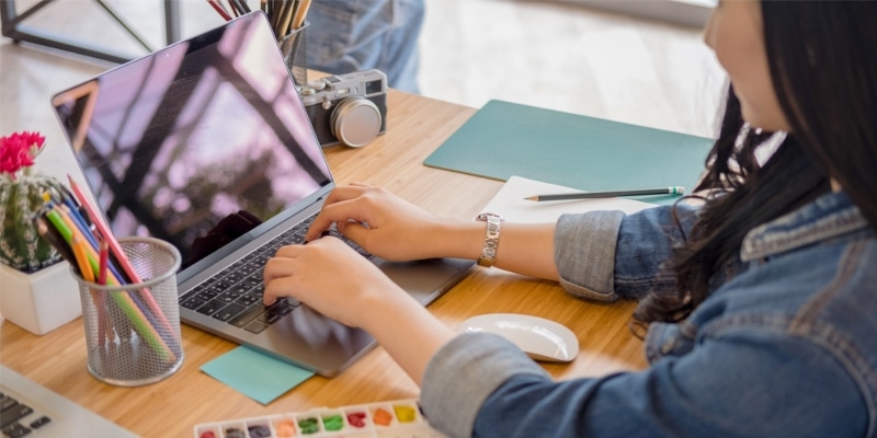 Why Use WordPress For Blogging Header Image Of Woman Typing On Laptop With Art Tools On The Desk