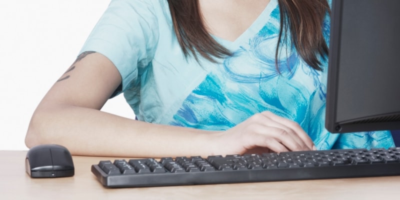 Female blogger with blue t-shirt using black keyboard, mouse & monitor